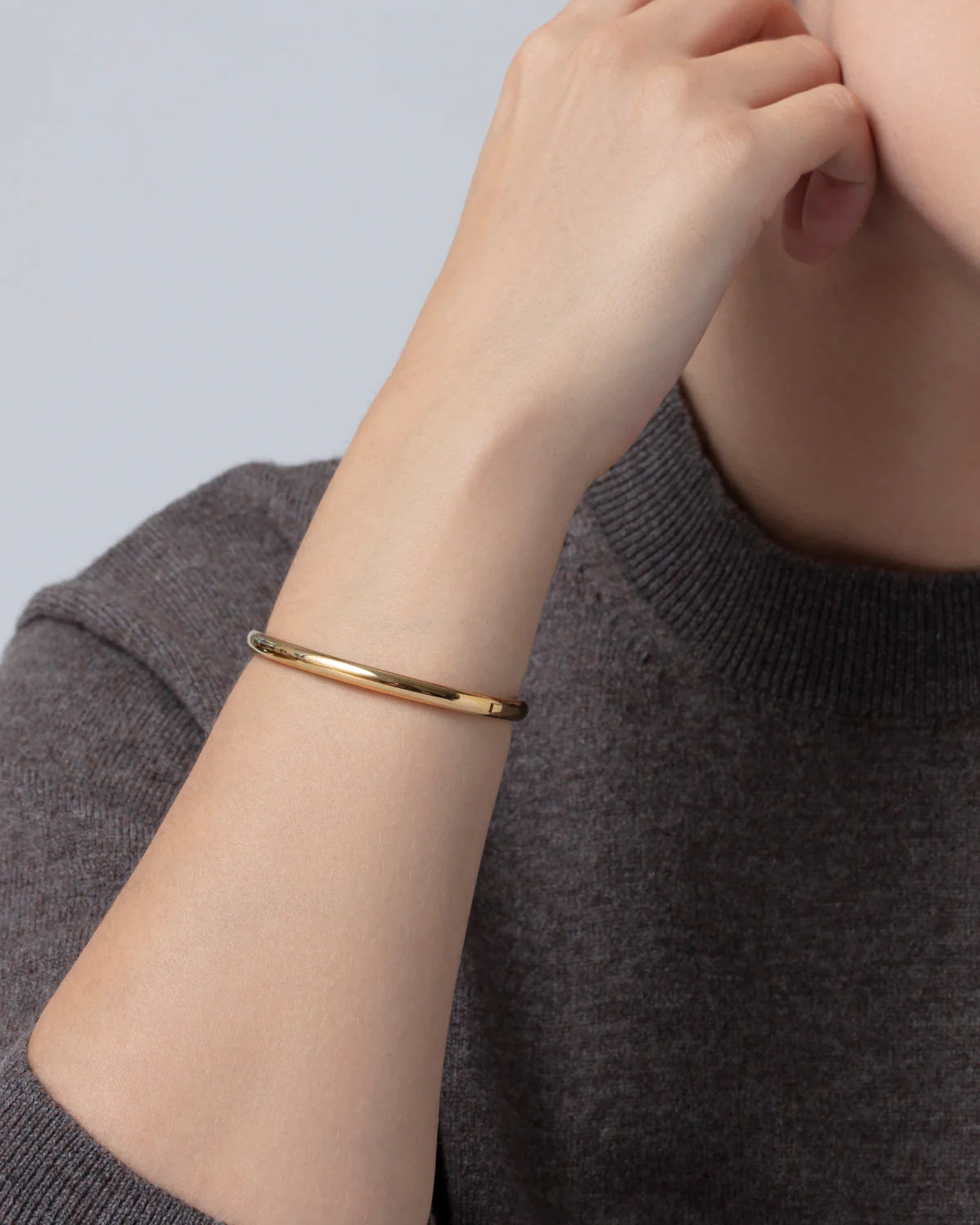 Gold bracelet on a person's wrist with a neutral background