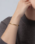 Gold bracelet on a person's wrist with a neutral background