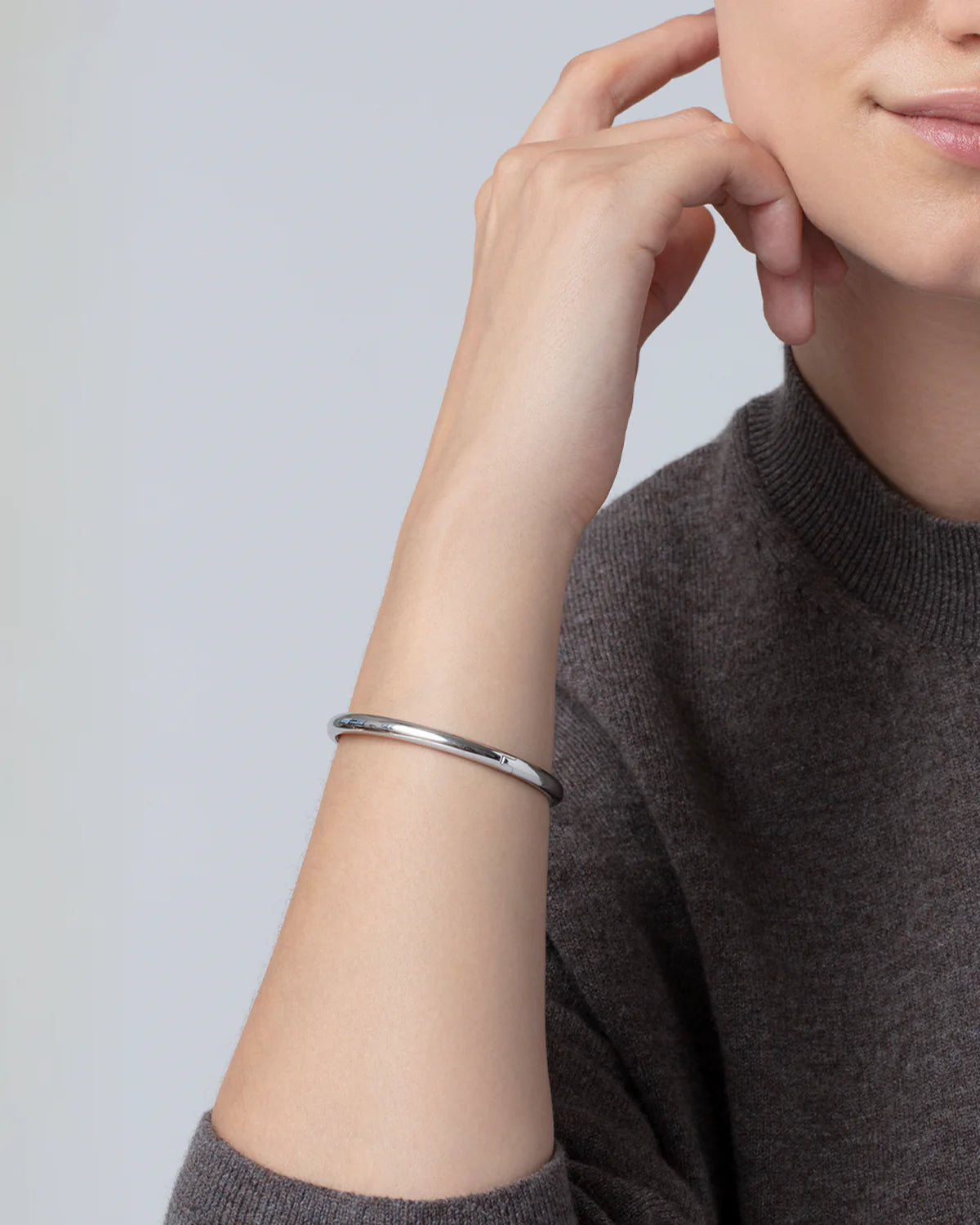 Person wearing a silver bracelet on a plain background