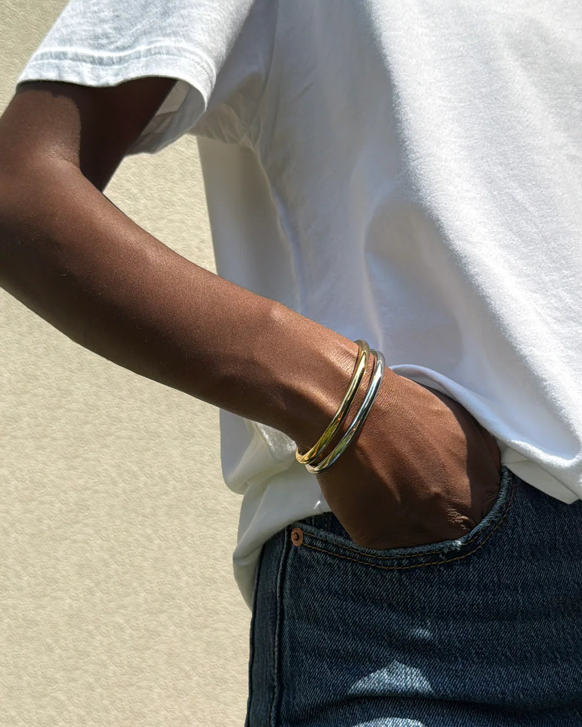 Person wearing a gold bracelet on a neutral background