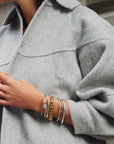 Person wearing a gray coat with multiple bracelets on a neutral background