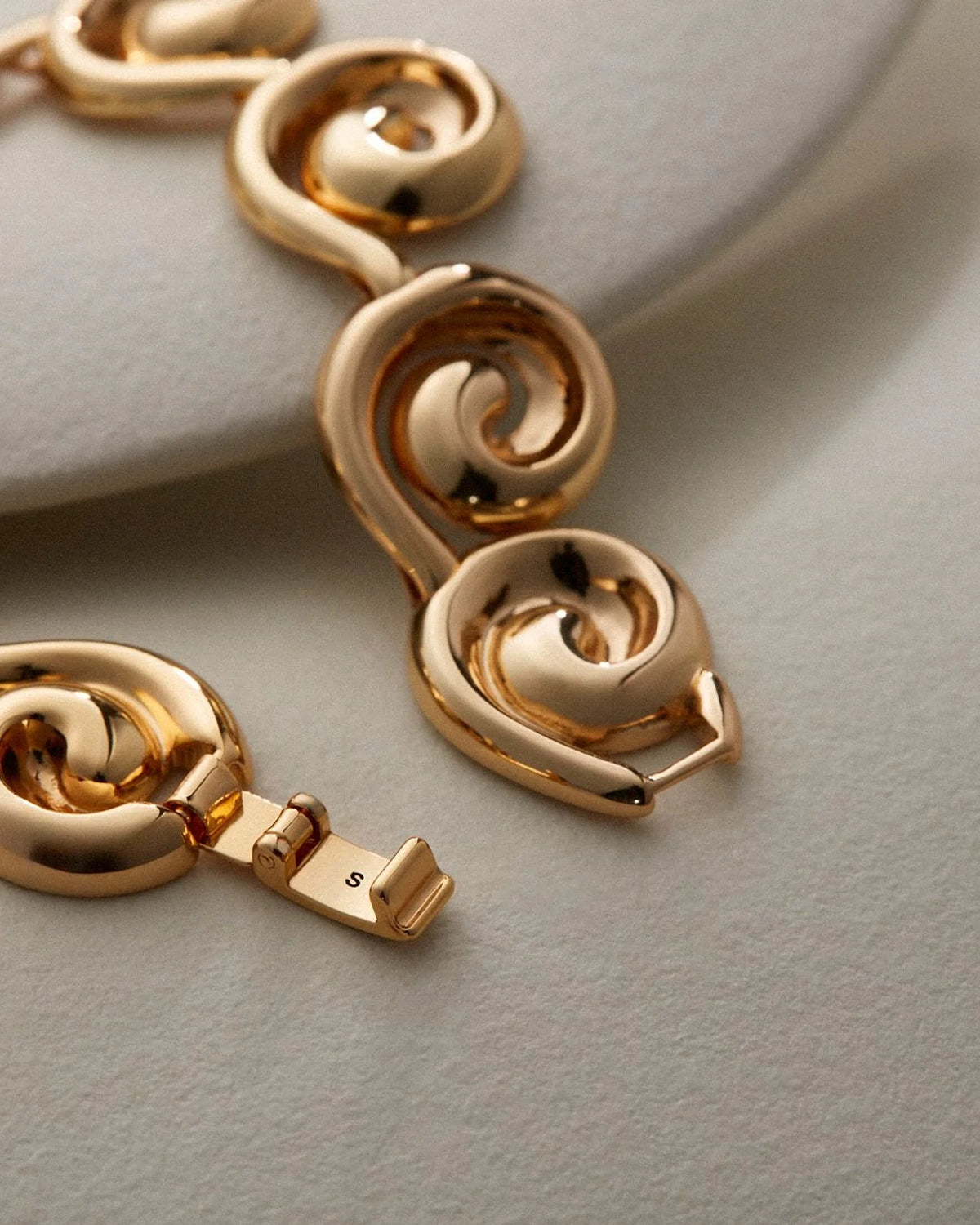 Gold-toned metal chain with thick, polished spiral links resting on a light gray textured surface.