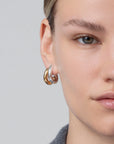 Close-up of a person wearing gold hoop earrings on a neutral background