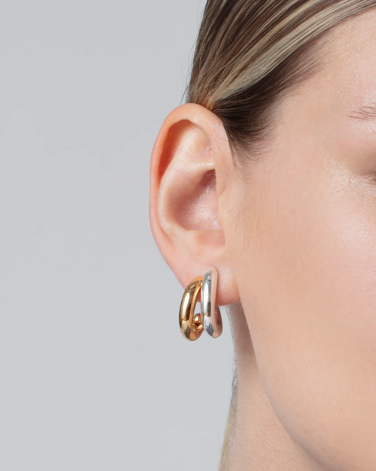 Close-up of an ear wearing gold hoop earrings on a neutral background