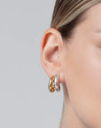 Close-up of an ear wearing gold hoop earrings on a neutral background