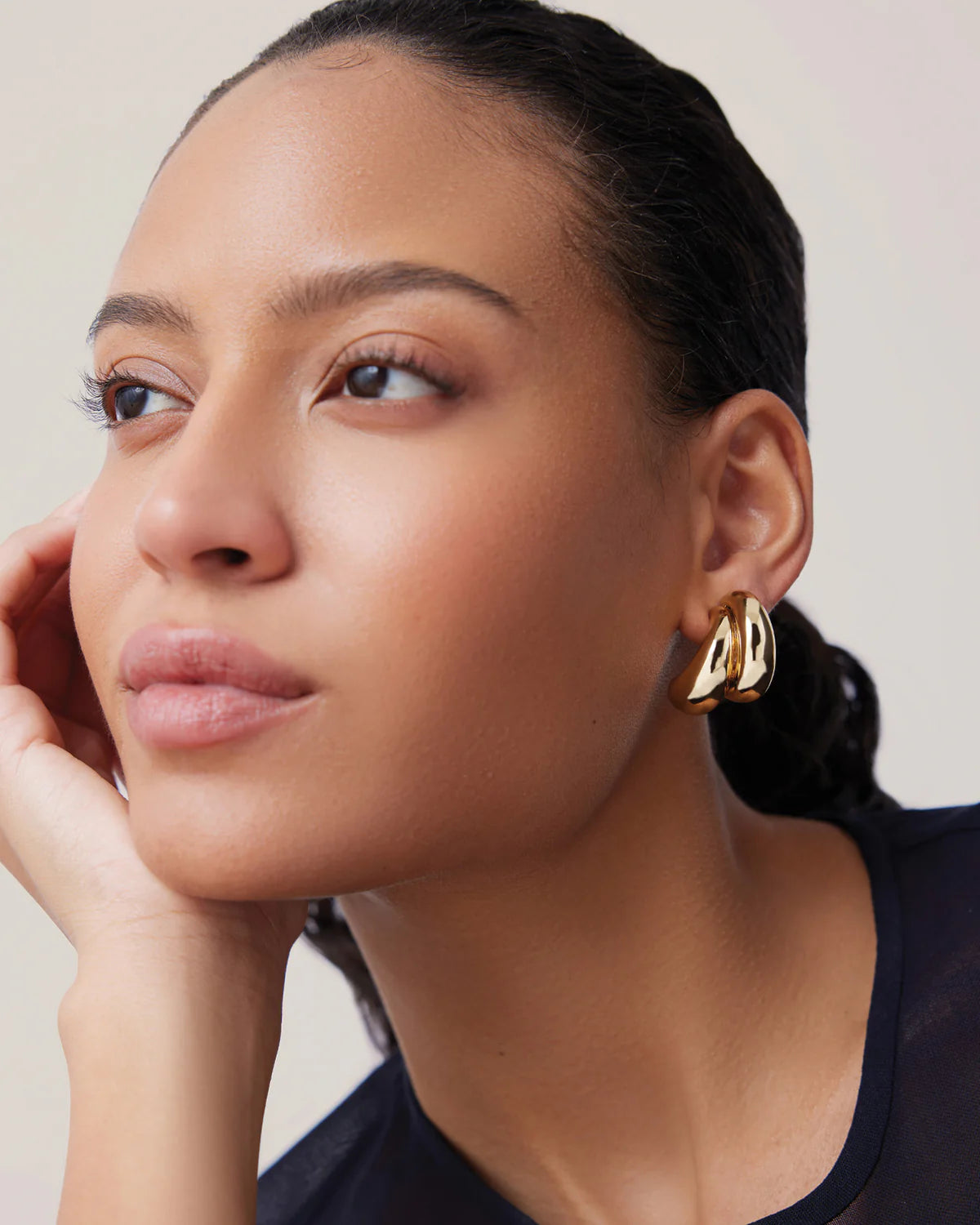 Woman wearing gold earrings with a neutral background