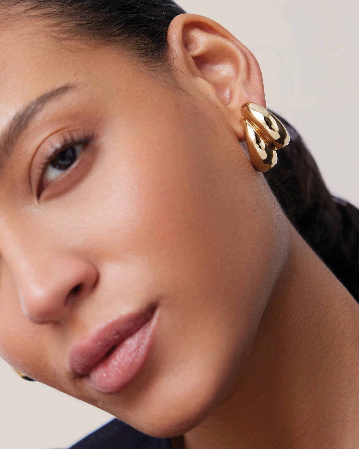 Close-up of a person wearing gold hoop earrings with a neutral background