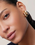 Close-up of a person wearing gold hoop earrings with a neutral background