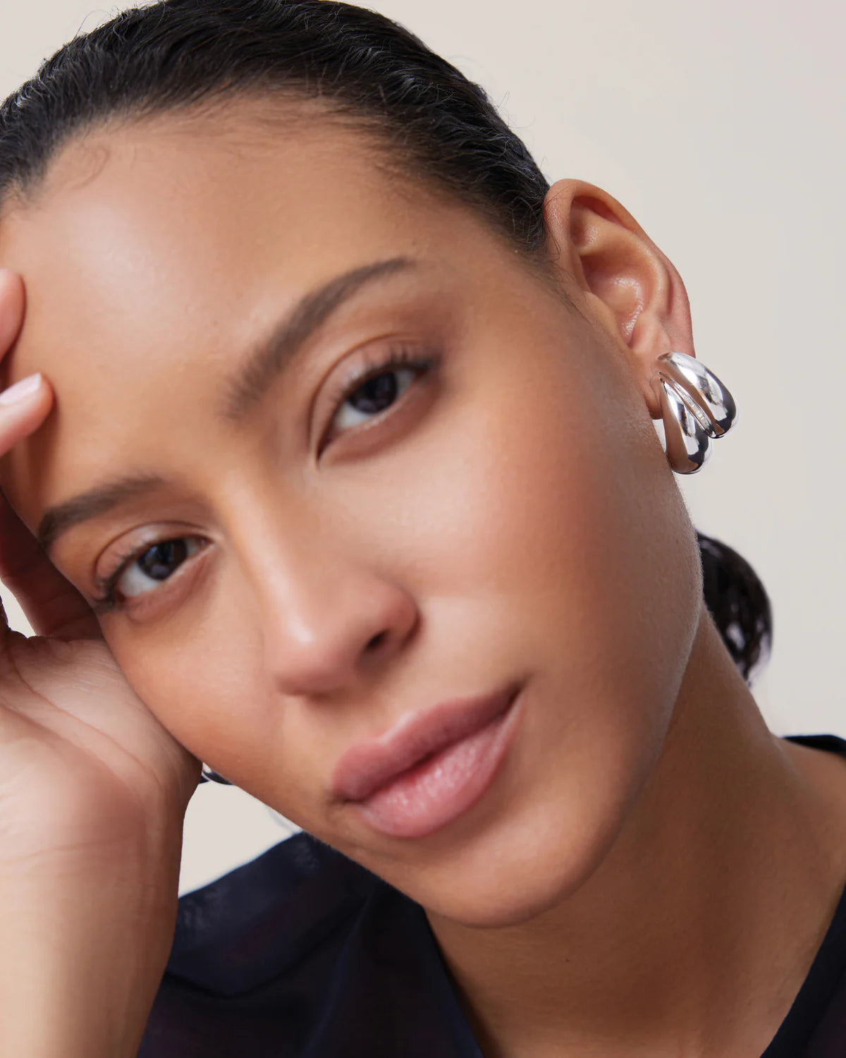 Close-up of a person wearing a silver hoop earring against a neutral background