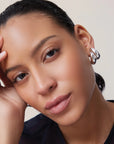 Close-up of a person wearing a silver hoop earring against a neutral background