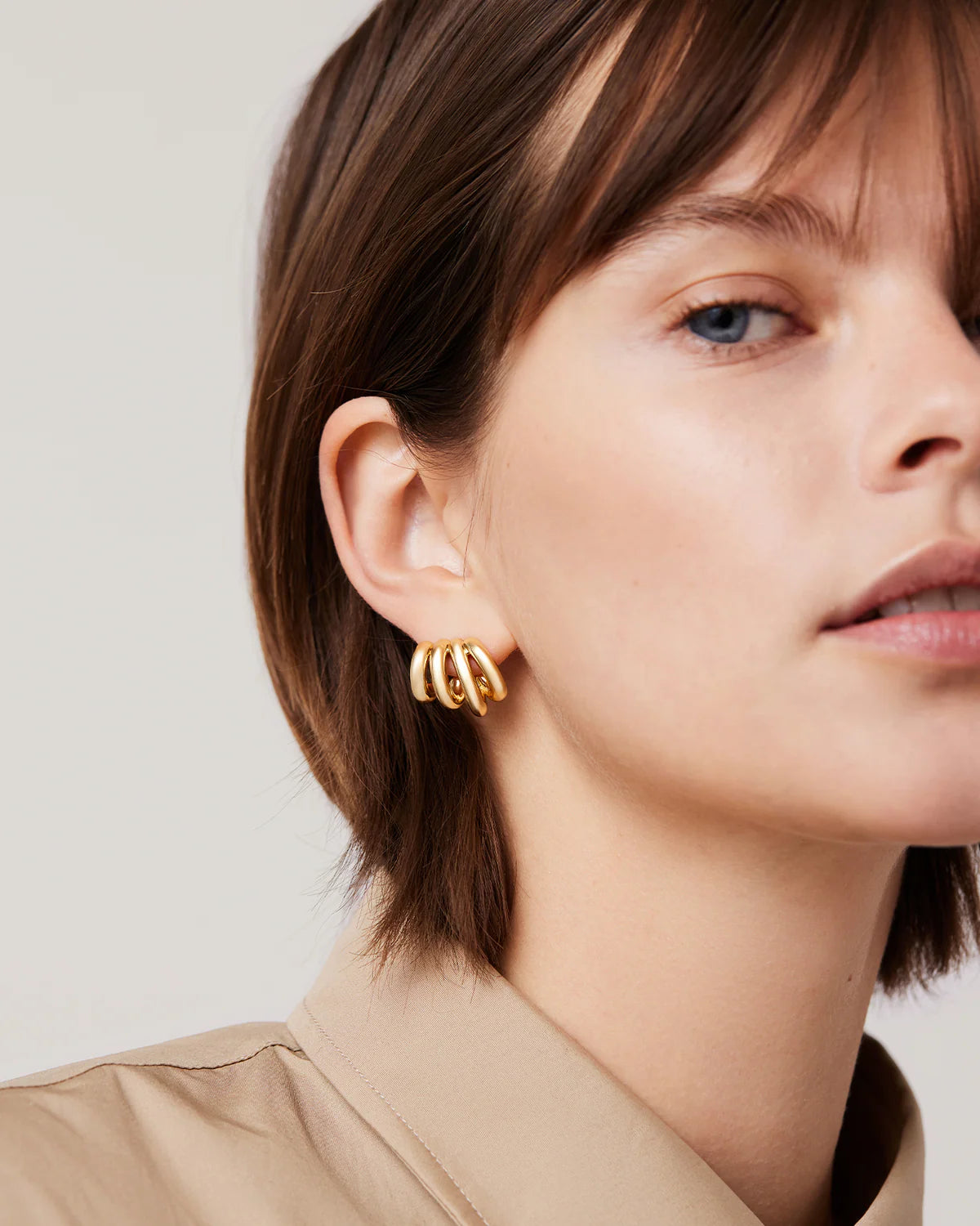 Close-up of a woman wearing gold hoop earrings against a neutral background