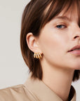 Close-up of a woman wearing gold hoop earrings against a neutral background