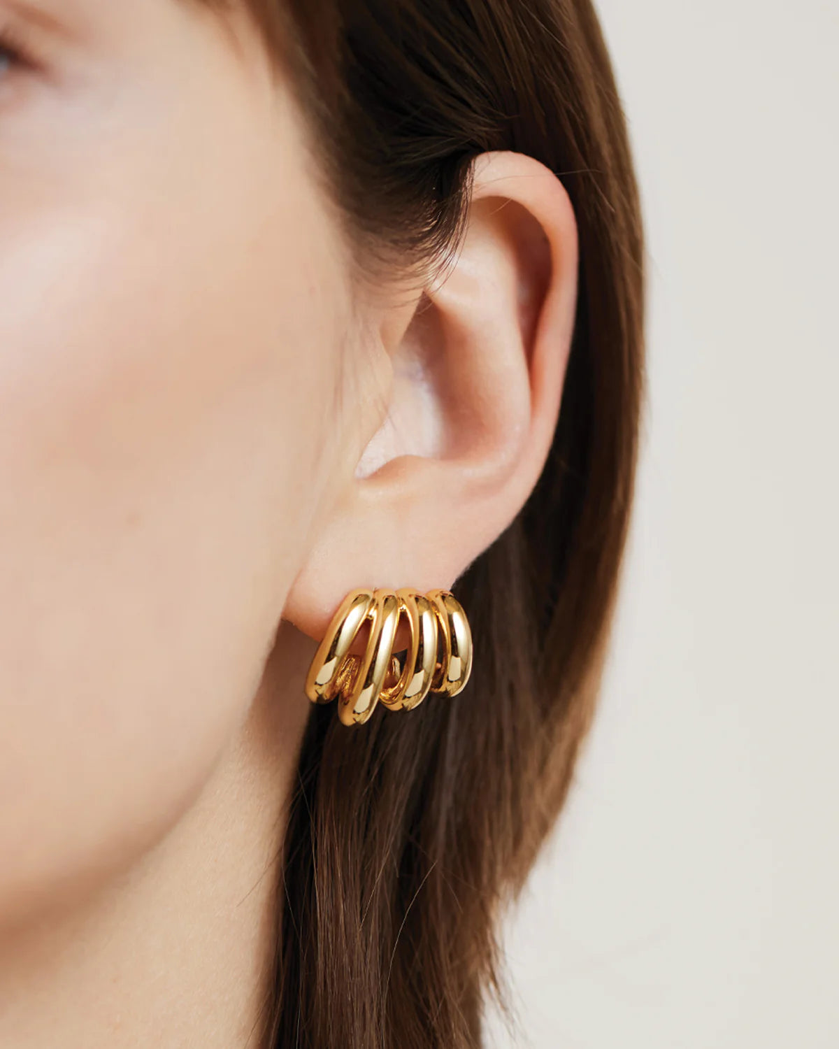 Gold hoop earring worn by a person with a neutral background