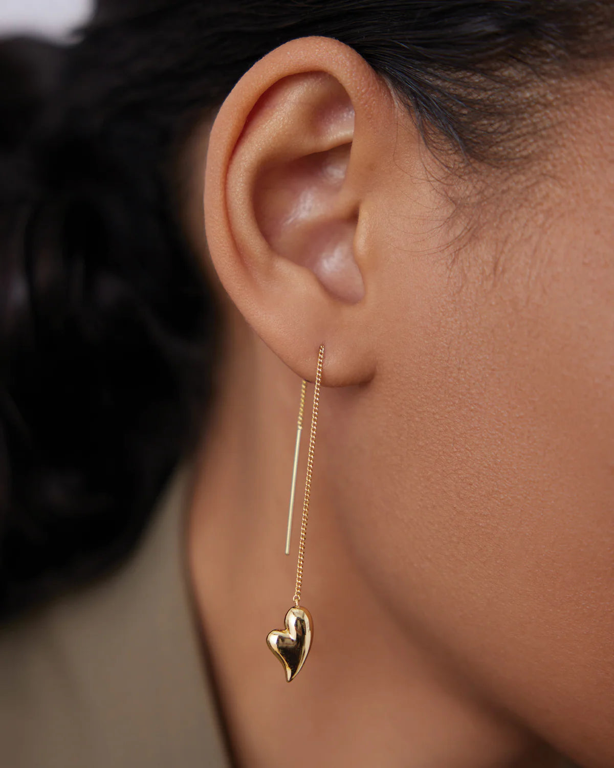 Gold heart-shaped earring worn by a person