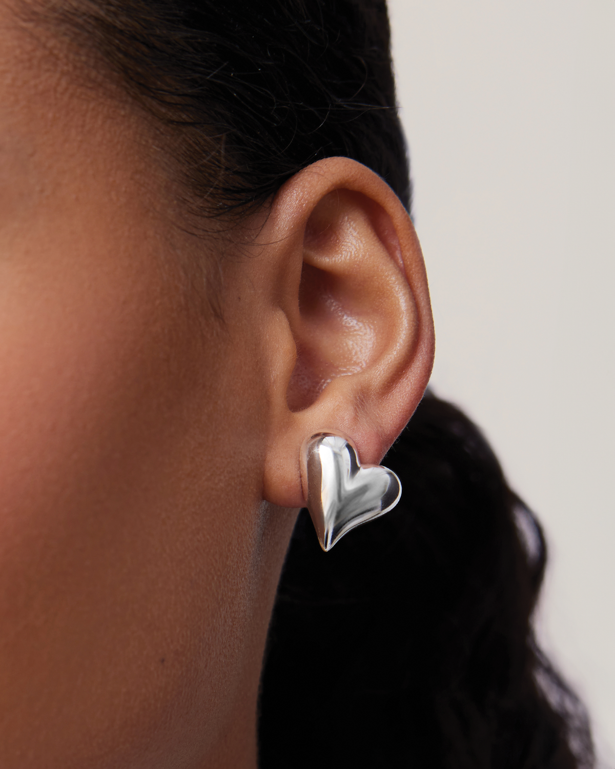 Silver heart-shaped earring worn by a person with a neutral background