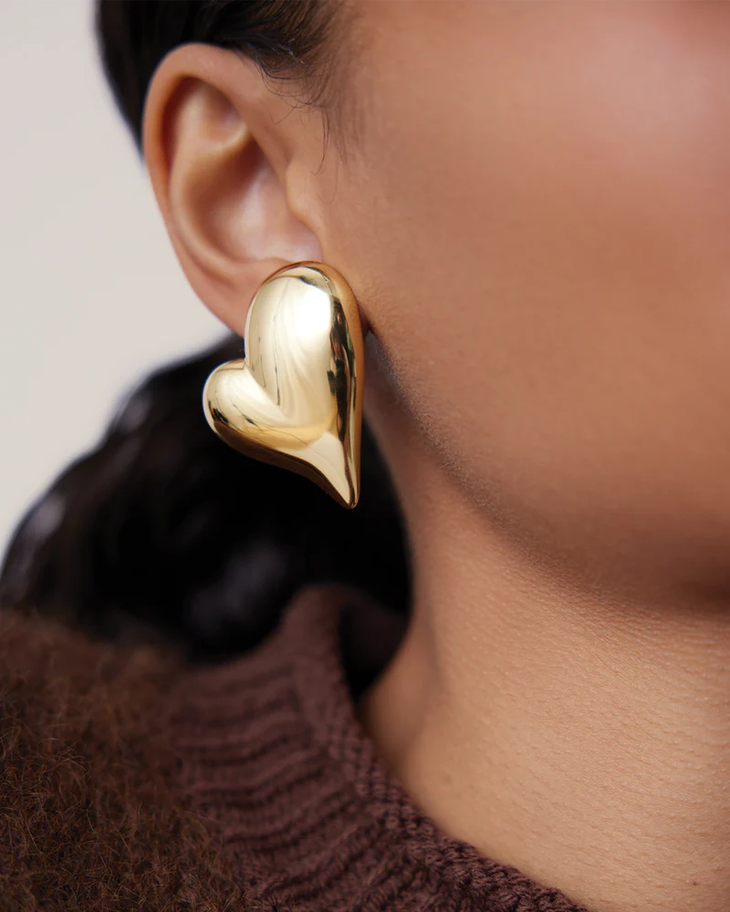 Gold heart-shaped earring worn by a person with a blurred background