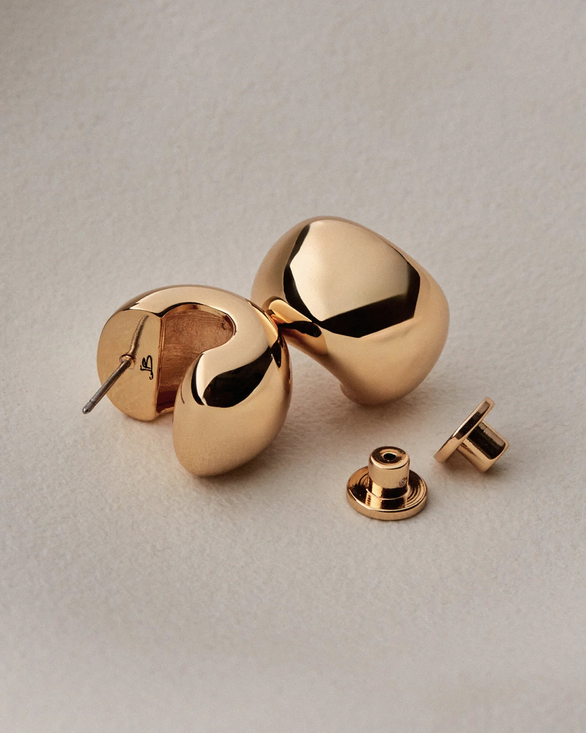 small, polished gold crescent-shaped stud earring against a light gray background.