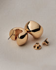 small, polished gold crescent-shaped stud earring against a light gray background.