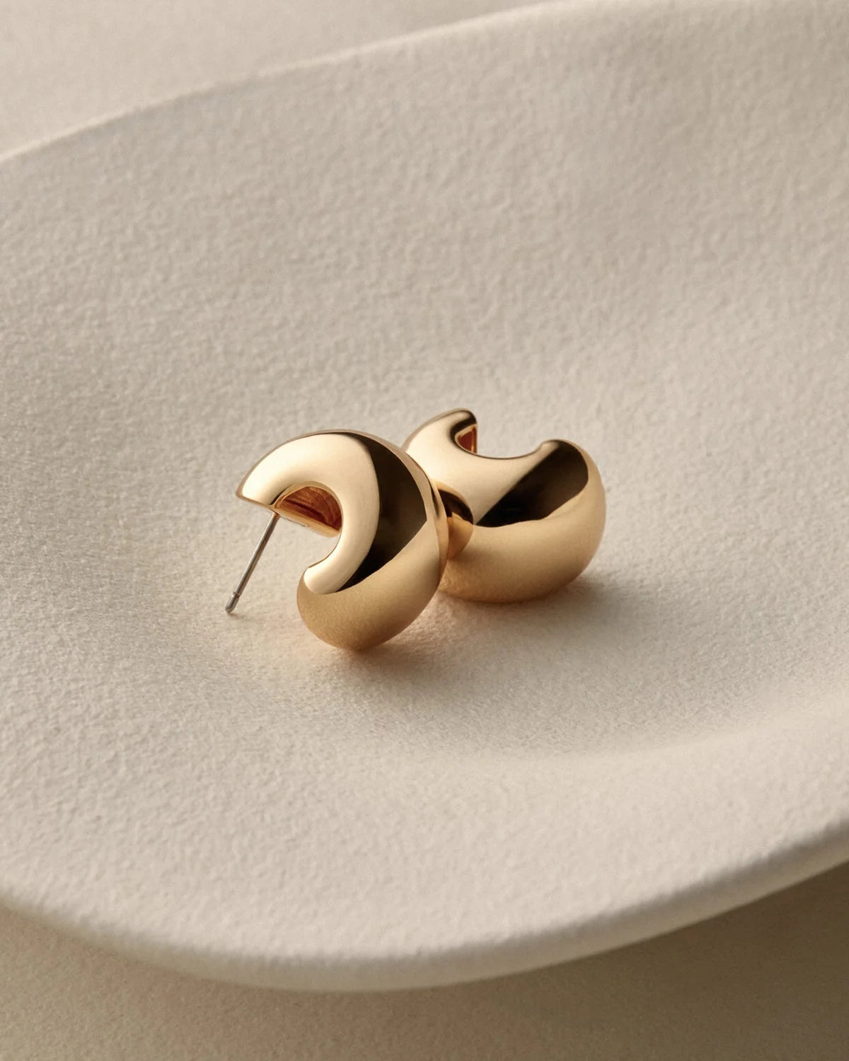 small, polished gold crescent-shaped stud earring against a light gray background.