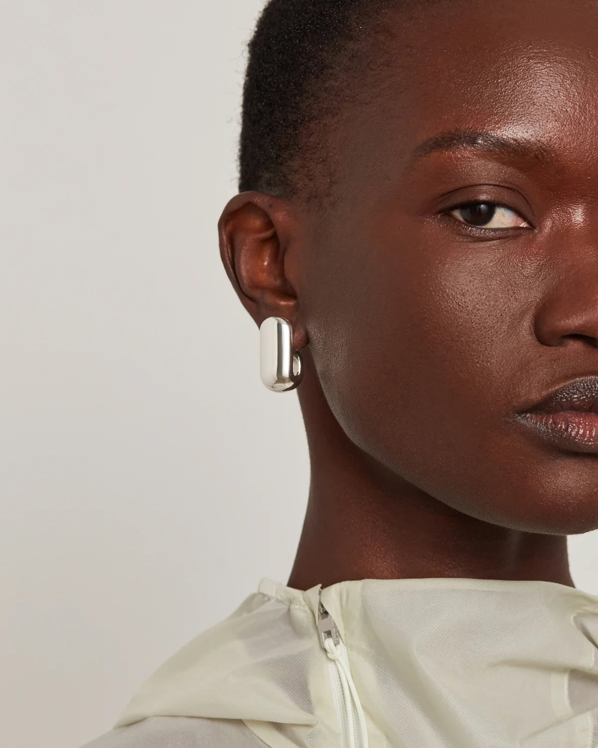 Close-up of a model wearing a single silver-toned geometric stud earring with a polished rectangular bar design.
