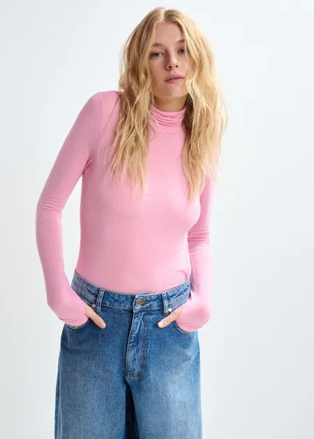 Person wearing a pink long-sleeve top and blue jeans on a white background