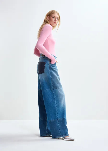 Woman wearing a pink top and blue patchwork jeans on a white background