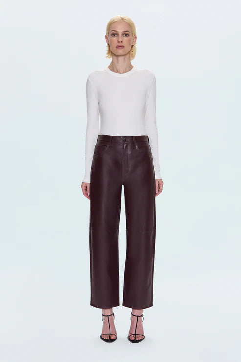 Person wearing a white long-sleeve top and brown leather pants on a white background front view