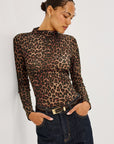 model wearing a long sleeve high neck leopard top with jeans on a grey background 