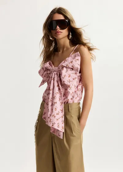 Woman wearing a pink floral top and beige pants with sunglasses on a white background