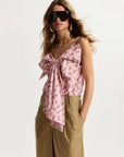 Woman wearing a pink floral top and beige pants with sunglasses on a white background