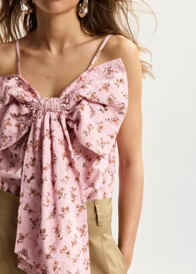Pink floral top with a bow detail worn by a person on a white background