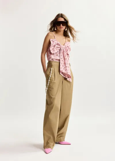 Woman wearing a pink floral top and beige pants on a white background