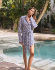 Woman in a striped dress standing by a pool with palm trees in the background