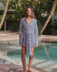 Woman in a blue striped dress standing by a pool with palm trees in the background