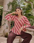 Woman in a striped red and white blouse and brown pants sitting outdoors.