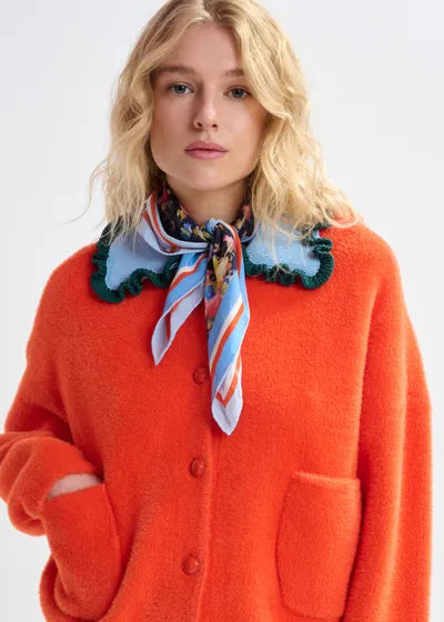 Person wearing an orange cardigan with a colorful scarf on a white background