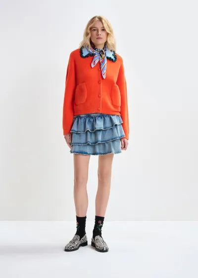 Person wearing an orange cardigan, denim skirt, and patterned scarf on a white background