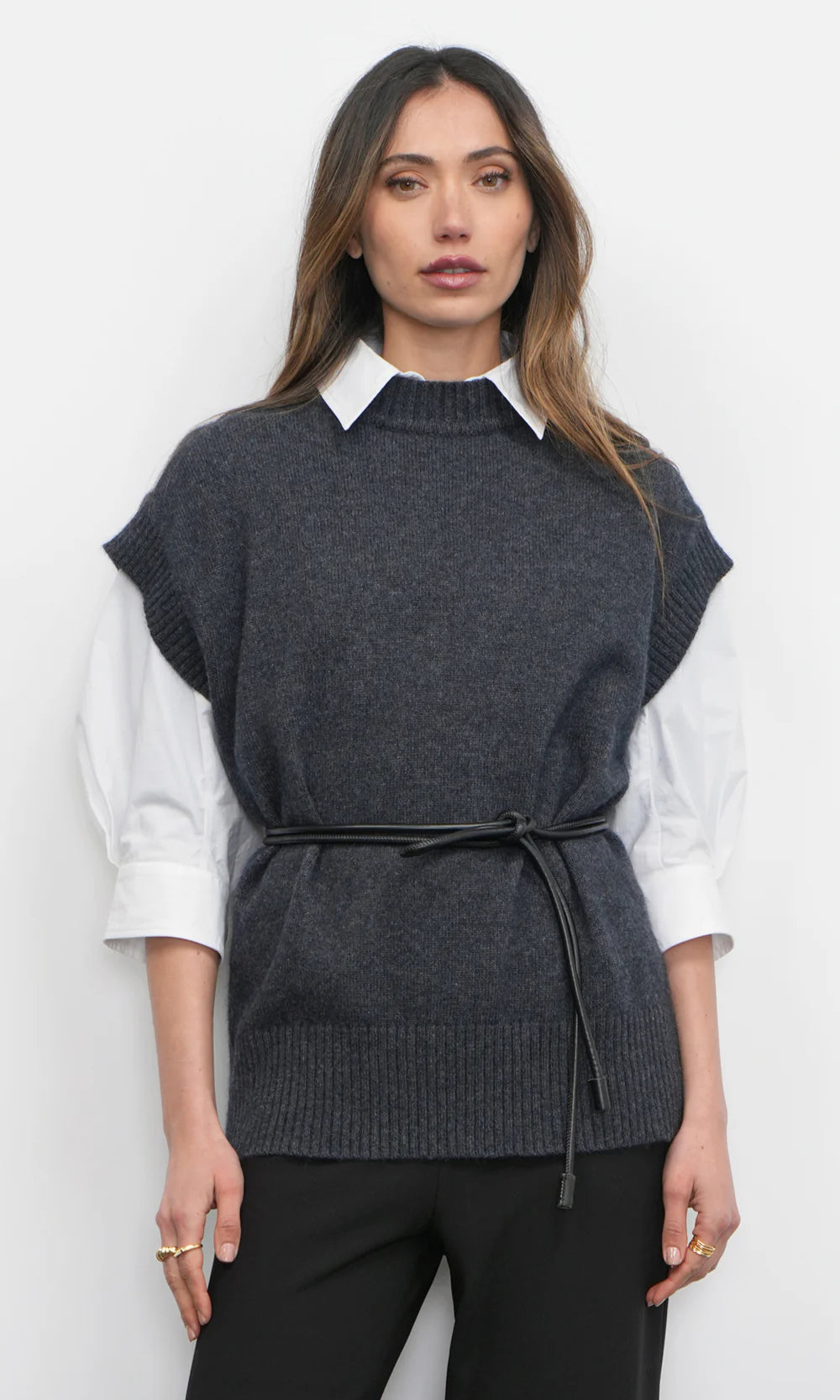 Woman wearing a dark gray sleeveless sweater vest over a white shirt on a white background