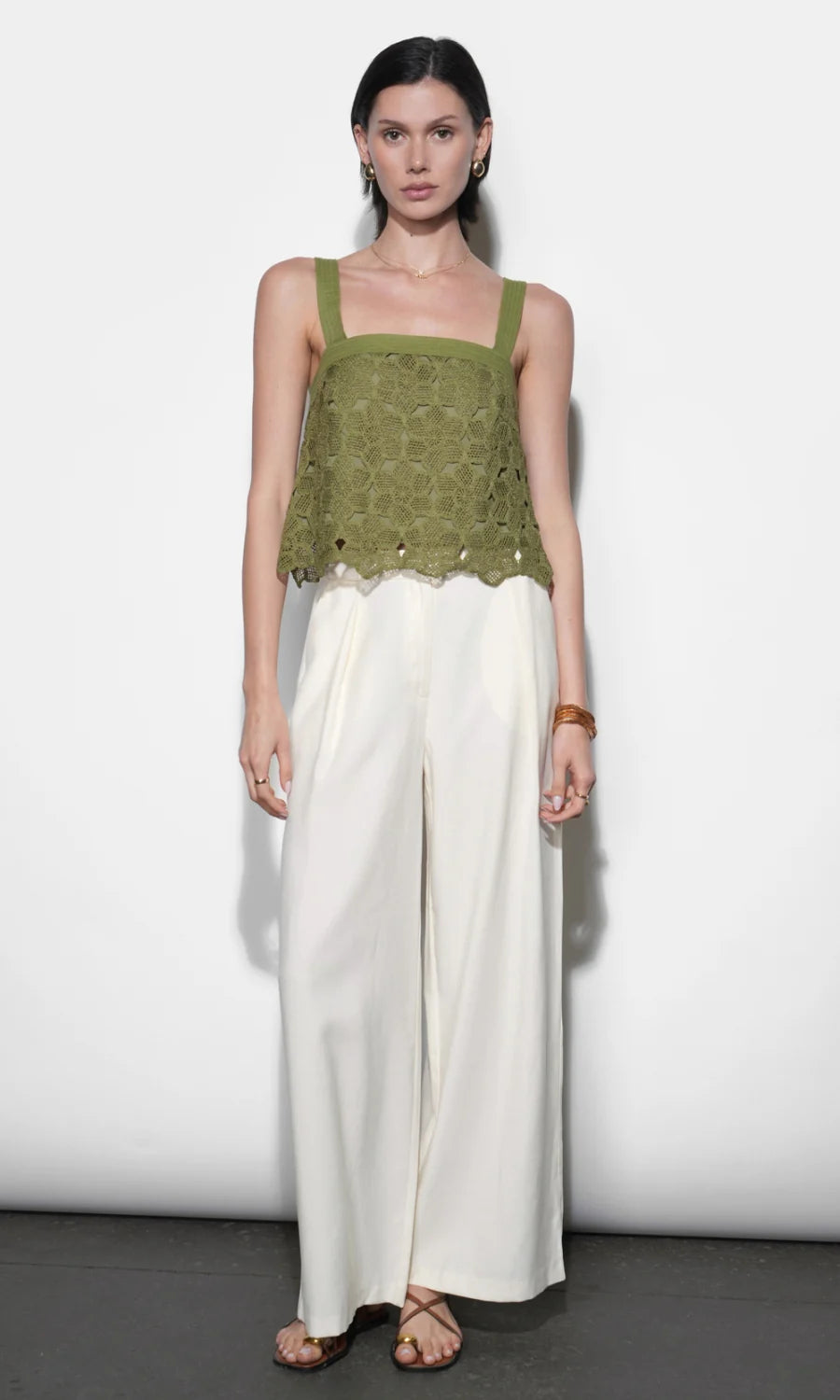 Woman wearing a green top and white pants against a white background