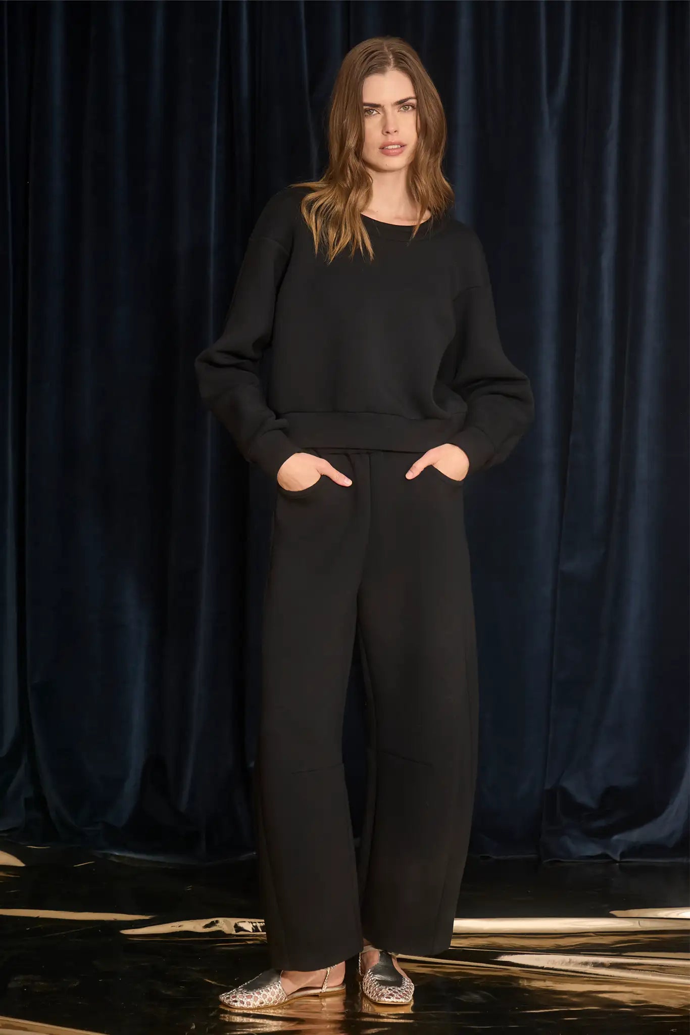 Woman wearing a black outfit against a dark blue curtain background