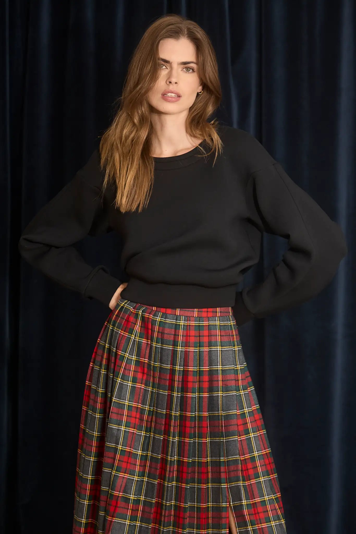 Woman wearing a black sweater and red plaid skirt against a dark background