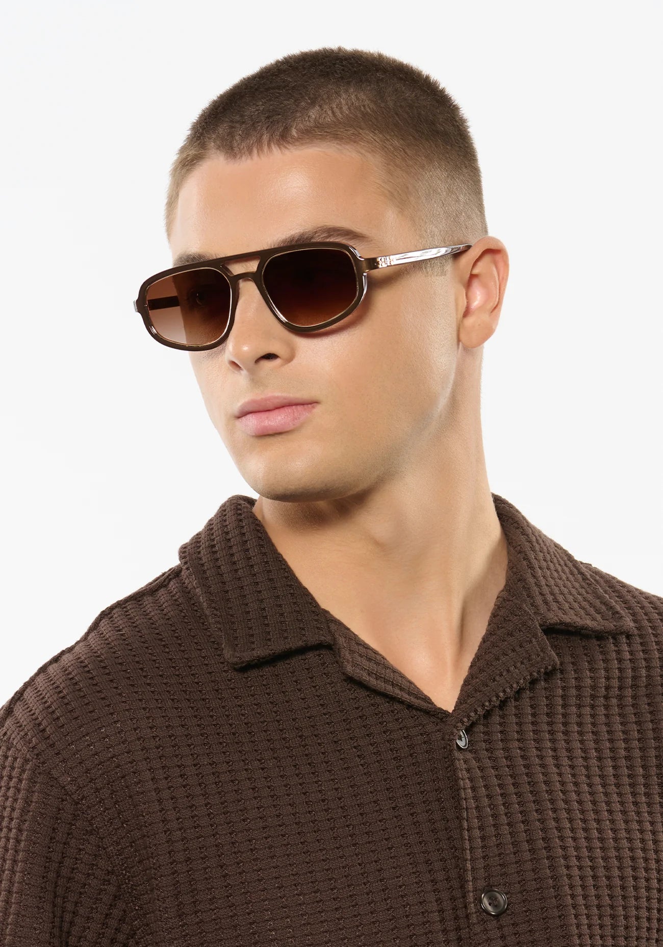 Man wearing brown sunglasses and a brown textured shirt against a white background