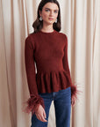 Woman wearing a rust-colored peplum sweater and blue jeans against a beige curtain background