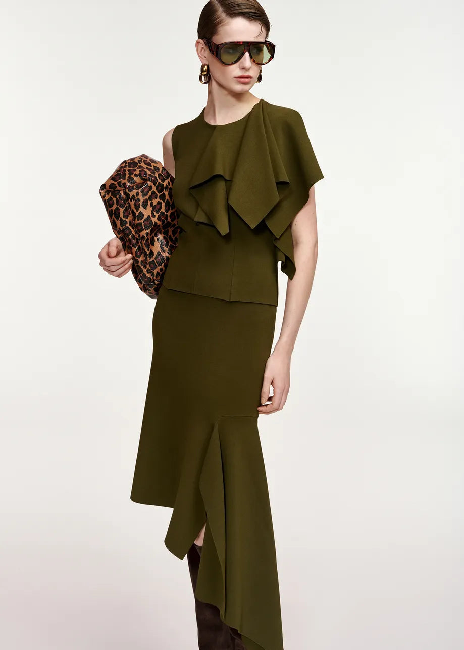 A model wearing an olive green two-piece set consisting of a sleeveless ruffled top and a matching asymmetrical skirt, holding a leopard print clutch against a plain light background.