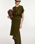 A model wearing an olive green two-piece set consisting of a sleeveless ruffled top and a matching asymmetrical skirt, holding a leopard print clutch against a plain light background.