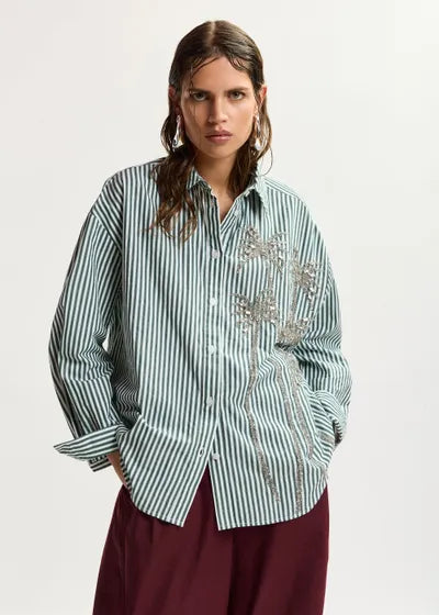 Woman wearing a green and white striped shirt with floral embellishments on a white background
