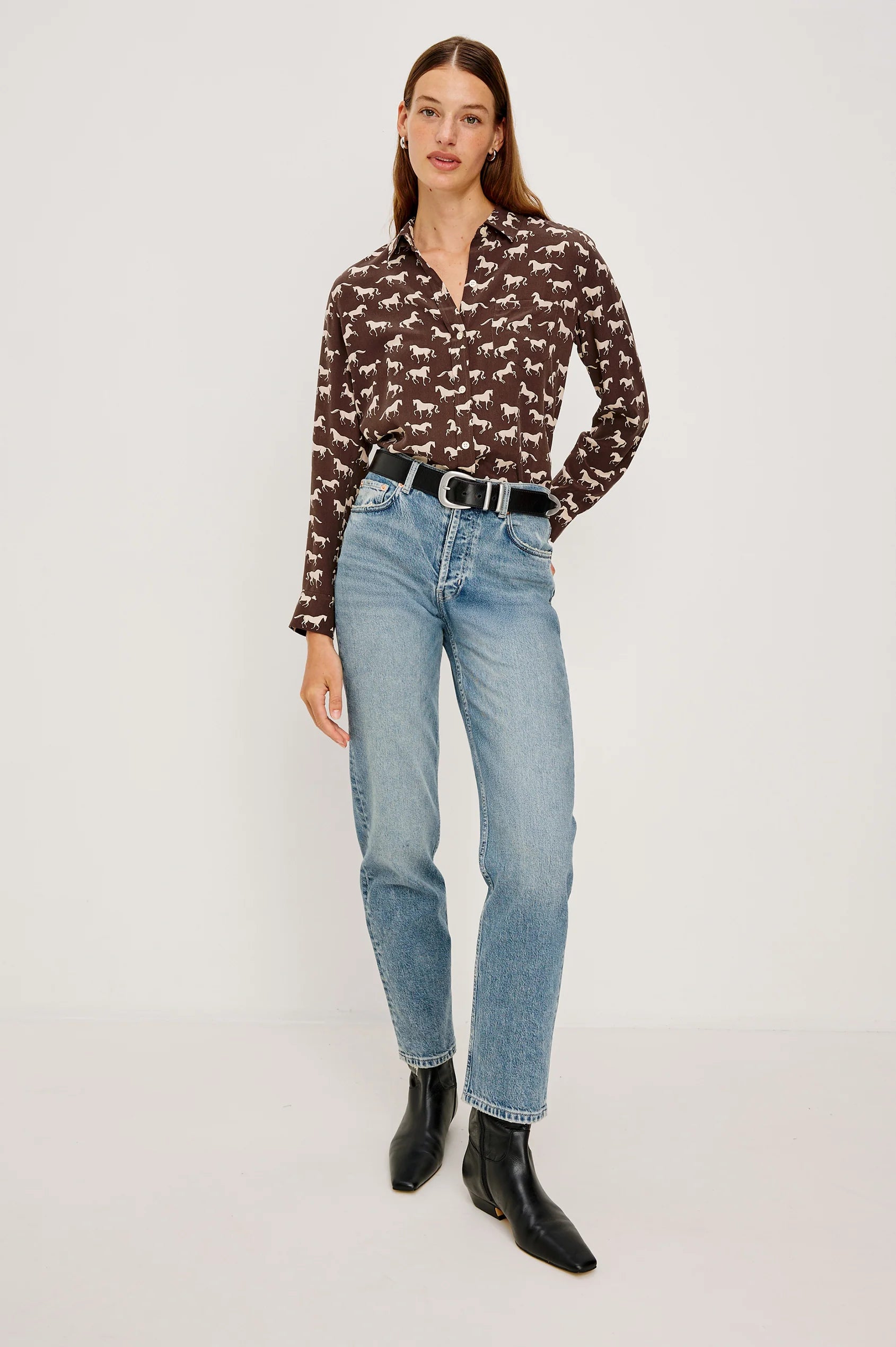 Woman wearing a patterned blouse, jeans, and black boots on a white background front view
