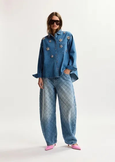 Person wearing a blue denim outfit with floral embellishments on a white background