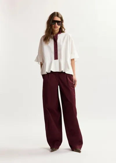 Woman wearing a white blouse with a maroon collar and burgundy pants on a white background