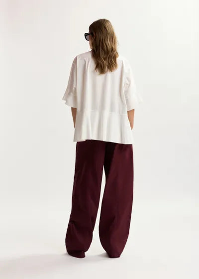 Person wearing a white top and burgundy pants on a light background
